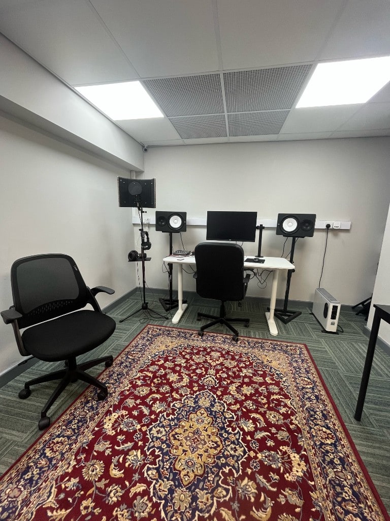 Wide view of Warrington Music Studio control room with Yamaha HS monitors, vocal booth, and patterned rug at Evans House.