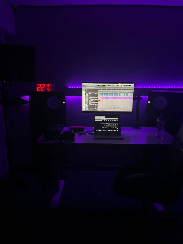 Production desk at Warrington Music Studio with laptop, DAW on screen, Yamaha monitors, headphones, and purple LED lighting.