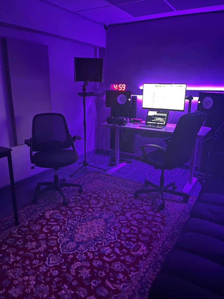 Warrington Music Studio control room with purple LED lighting, ergonomic chairs, patterned rug, and full monitoring setup.