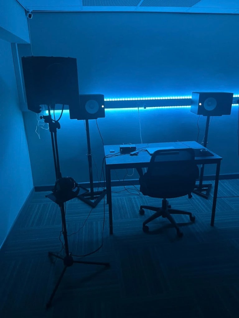 Blue-lit Warrington Music Studio room with desk, studio monitors, laptop, vocal reflection shield, and mic stand.